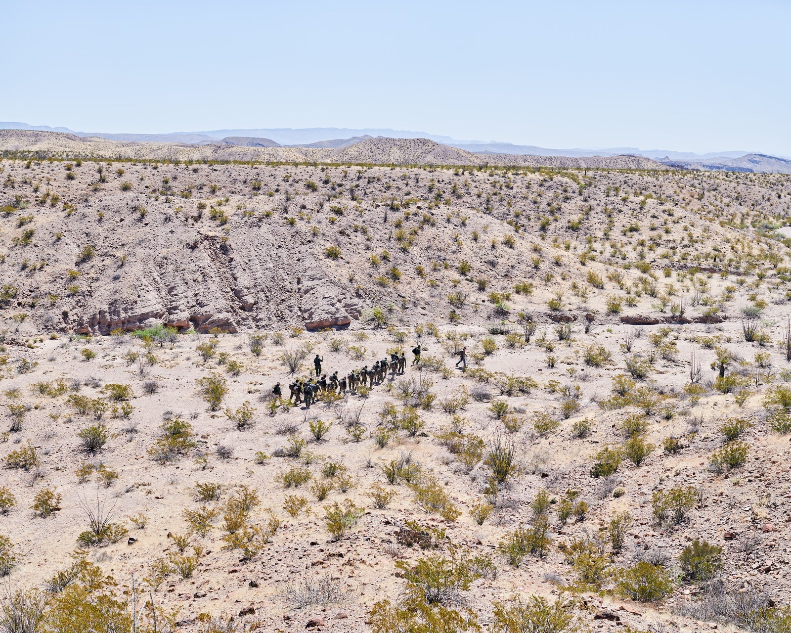The landscape of the southern border as seen from above with a group of people in the distance.