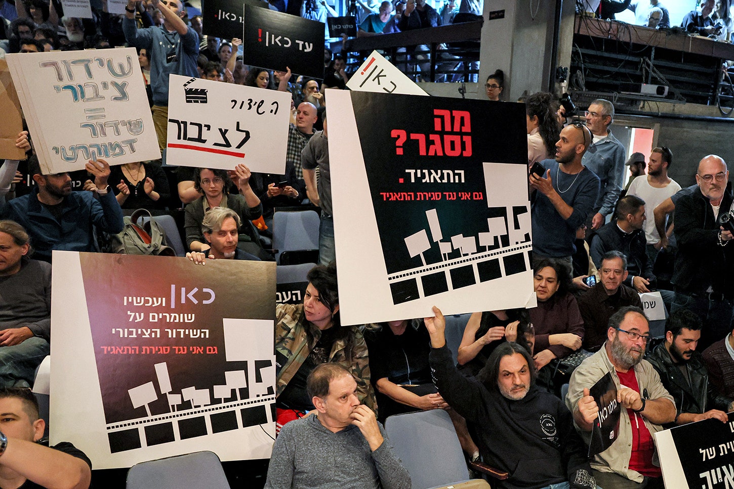 A group of people protest holding signs in Hebrew.